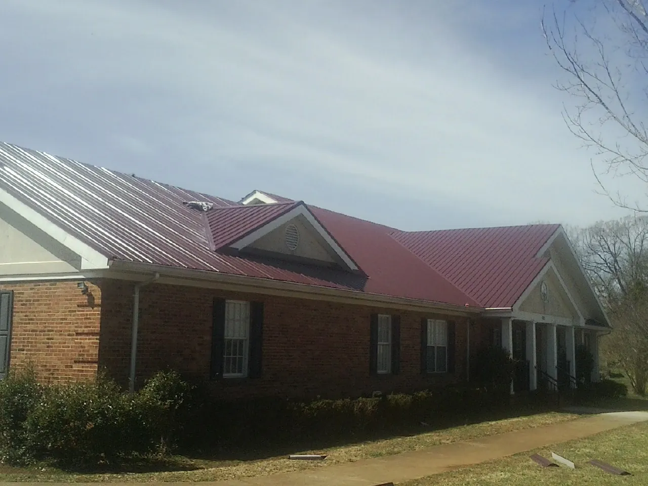 Red metal roof with gabled entries on a long brick building, from a Hail Damage Roof Repair job in Glenwood