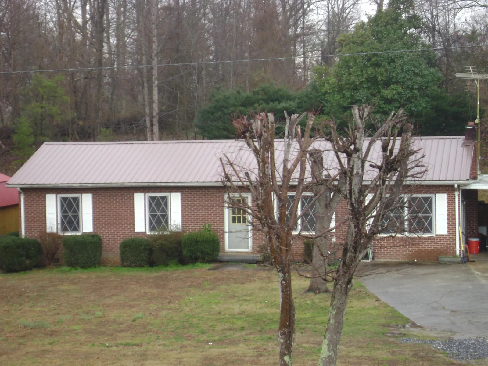 Mauve metal roof on a brick ranch home behind bare trees in Glenwood