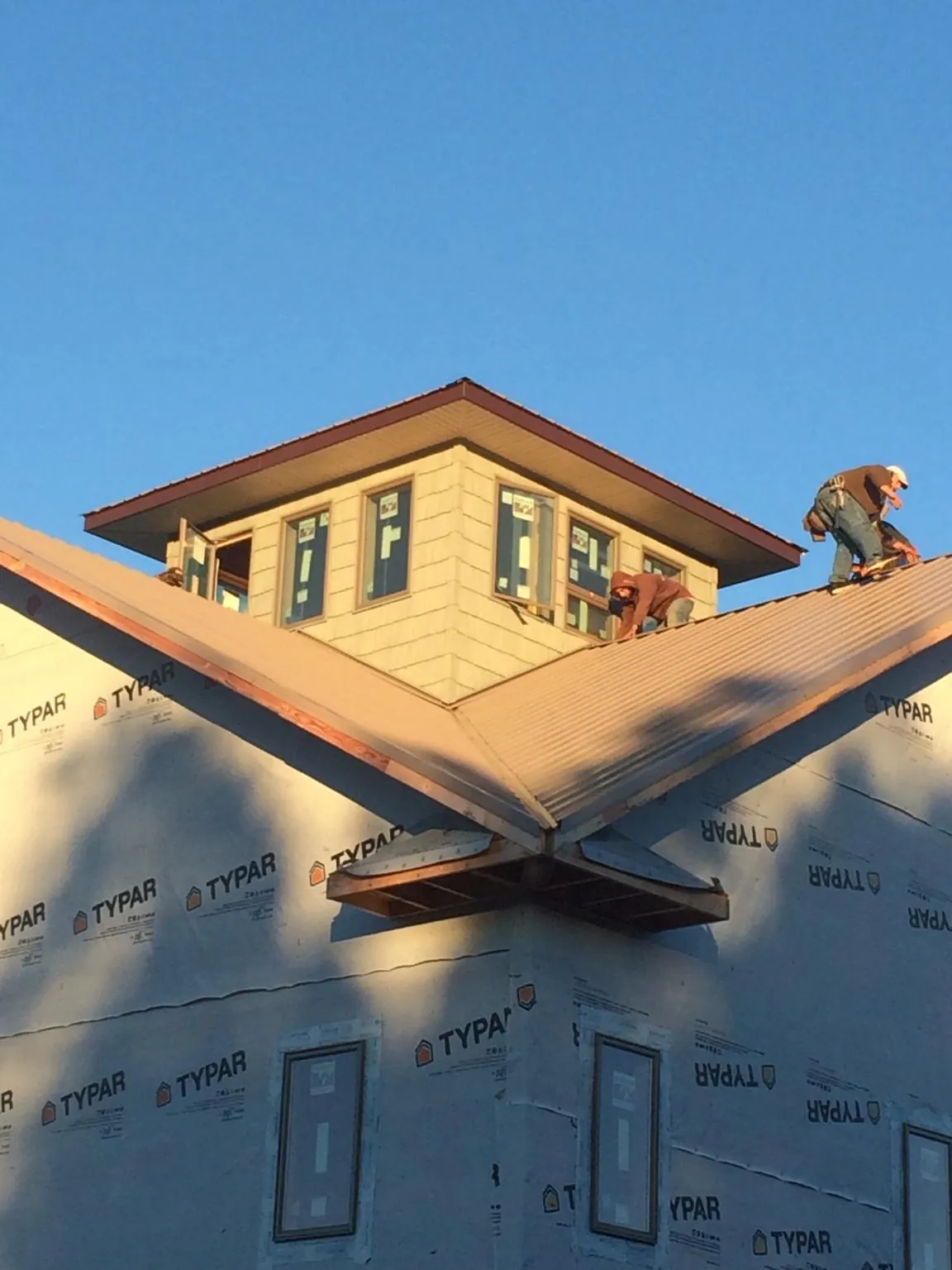 Roofers working around a rooftop cupola on a new metal roof at sunset — Roof Waterproofing in Glenwood by Roofing Brothers